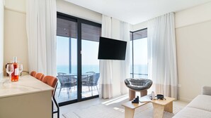 A modern hotel room with a balcony, a dining area, a seating area, and a TV.