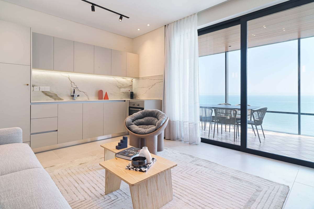 Una sala de estar moderna con un sofá, una mesa de centro y vista al océano a través de amplios ventanales.