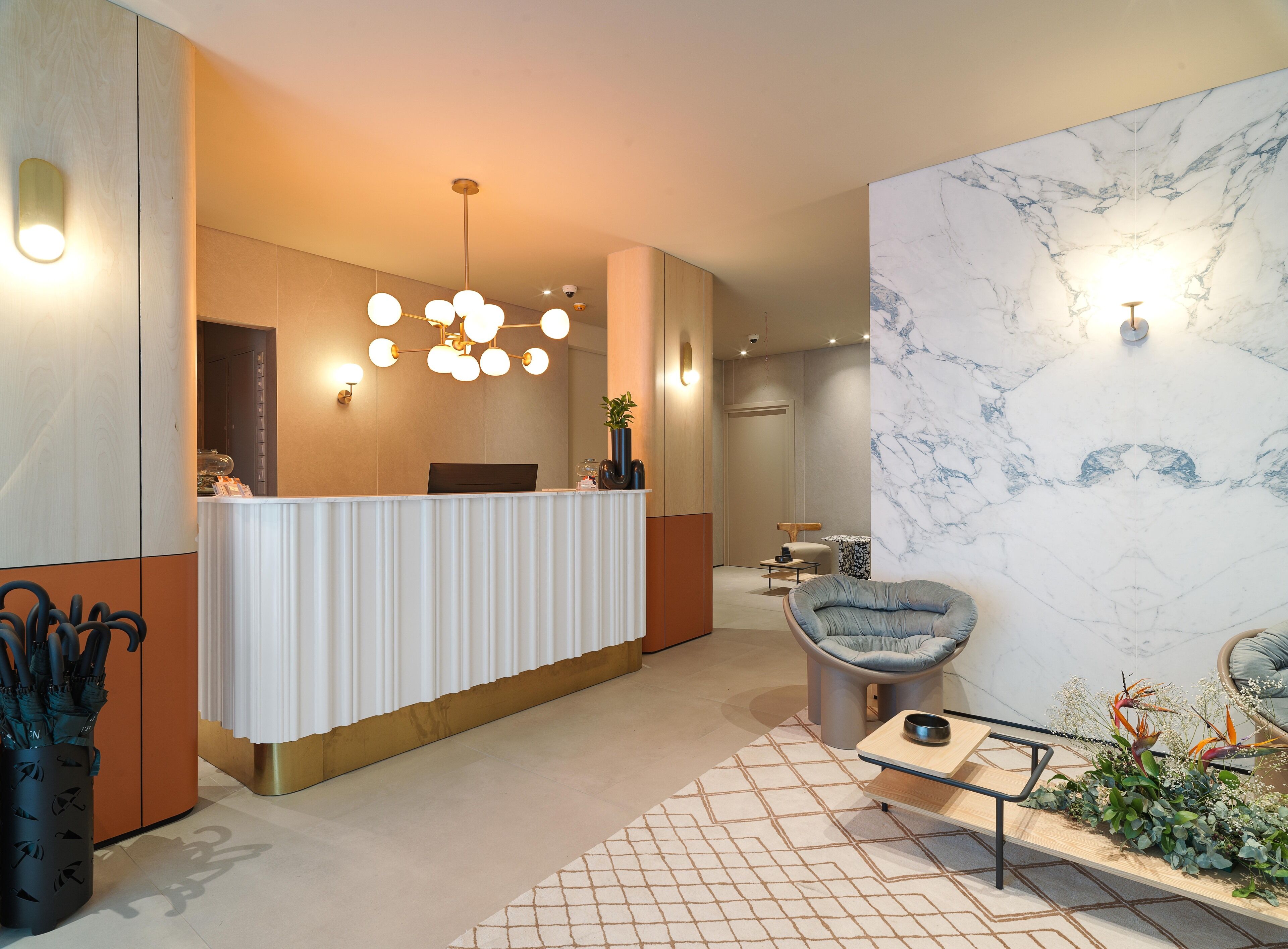 A modern reception area with a white reception desk, a seating area with a blue chair, and a marble wall.