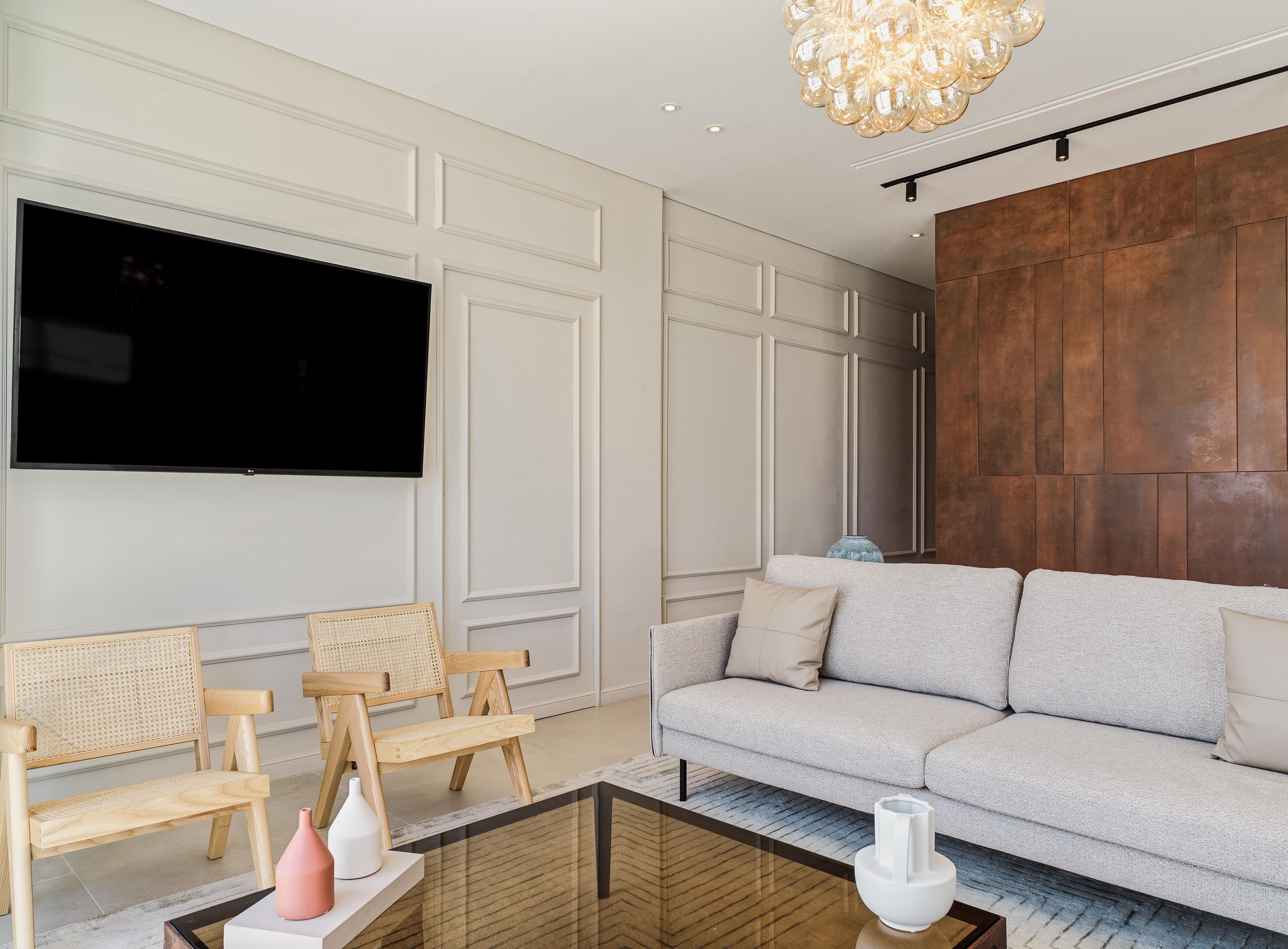 Ein modernes Wohnzimmer mit einem großen Flachbildfernseher, einem Holzsofa, zwei Korbstühlen und einem Couchtisch mit Dekoration.