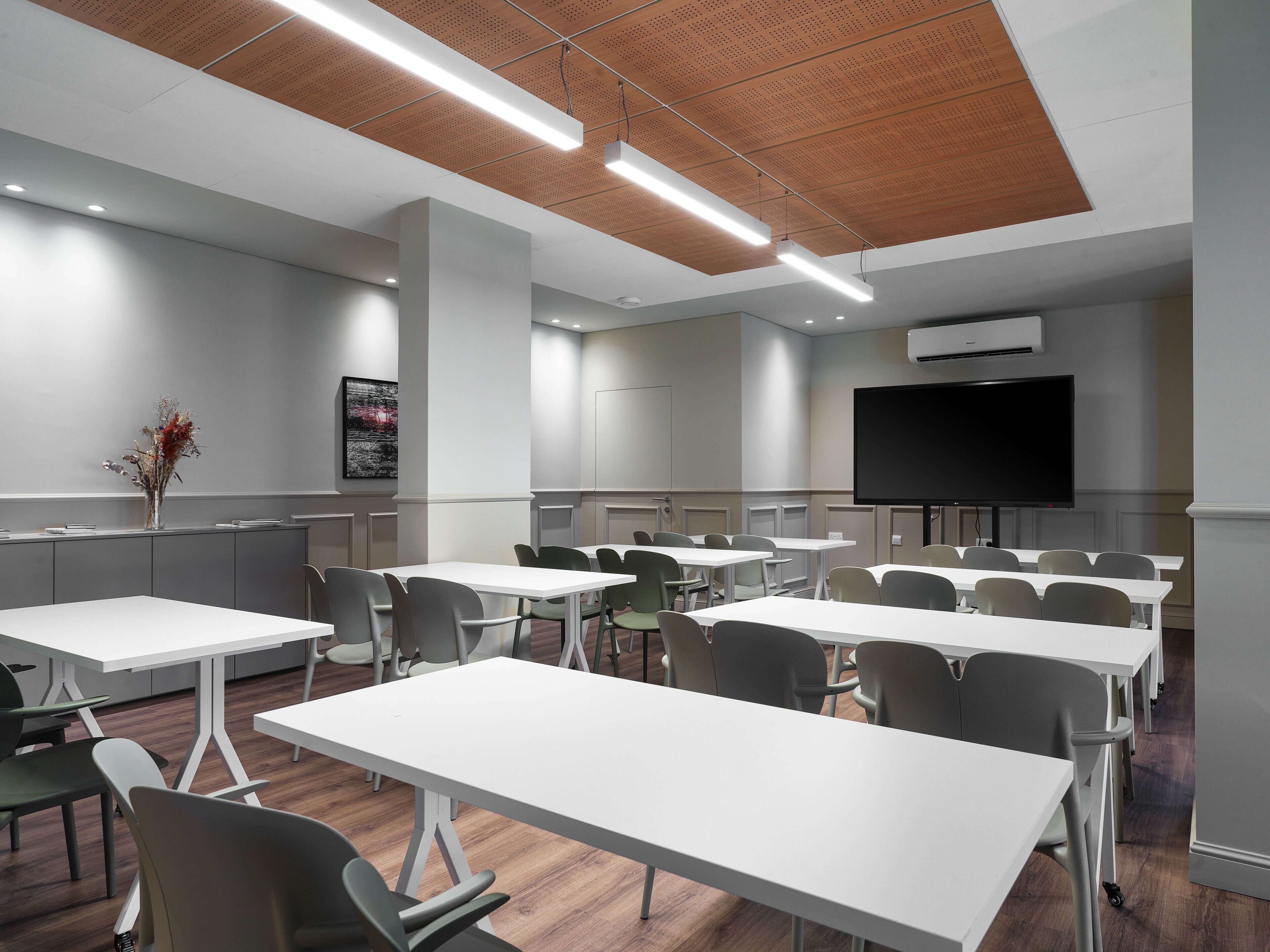 A conference room with white tables and chairs, a large screen, and an air conditioning unit.