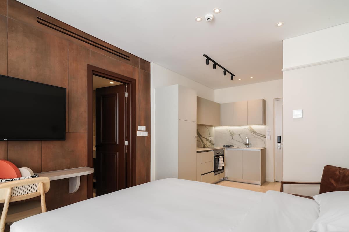 Una habitación de hotel con cama, televisión, puerta de madera, kitchenette y baño.