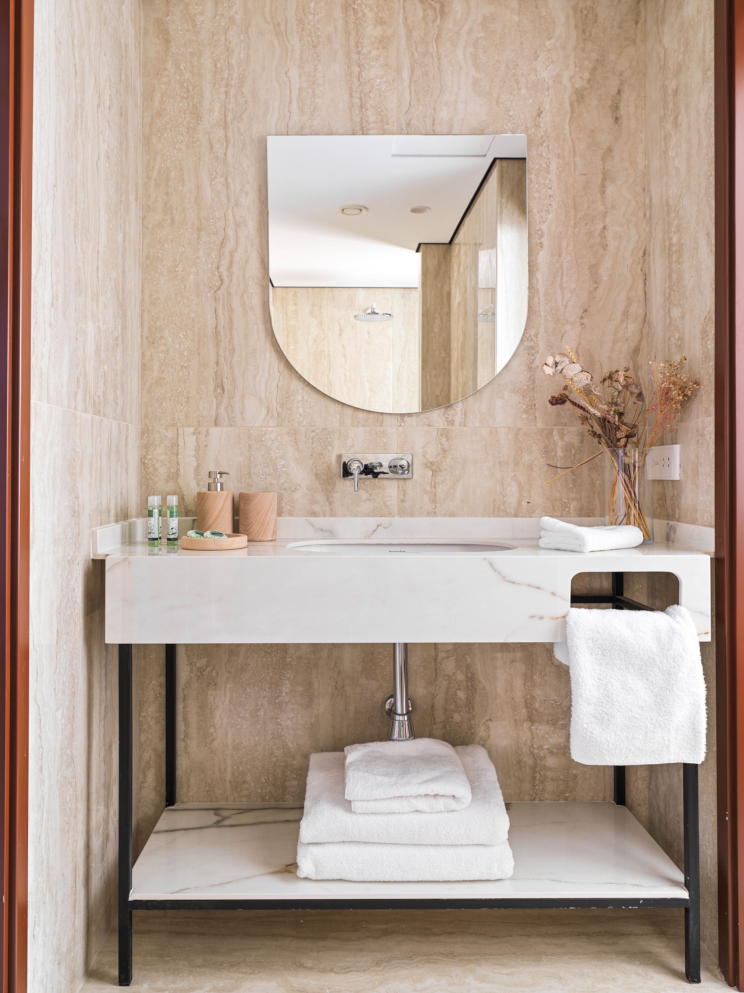 A bathroom with a marble sink, a mirror, a towel rack, and a vase with dried flowers.