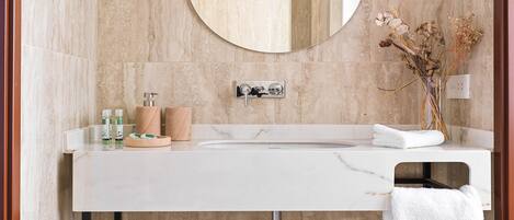 A bathroom with a marble sink, a mirror, a towel rack, and a vase with dried flowers.