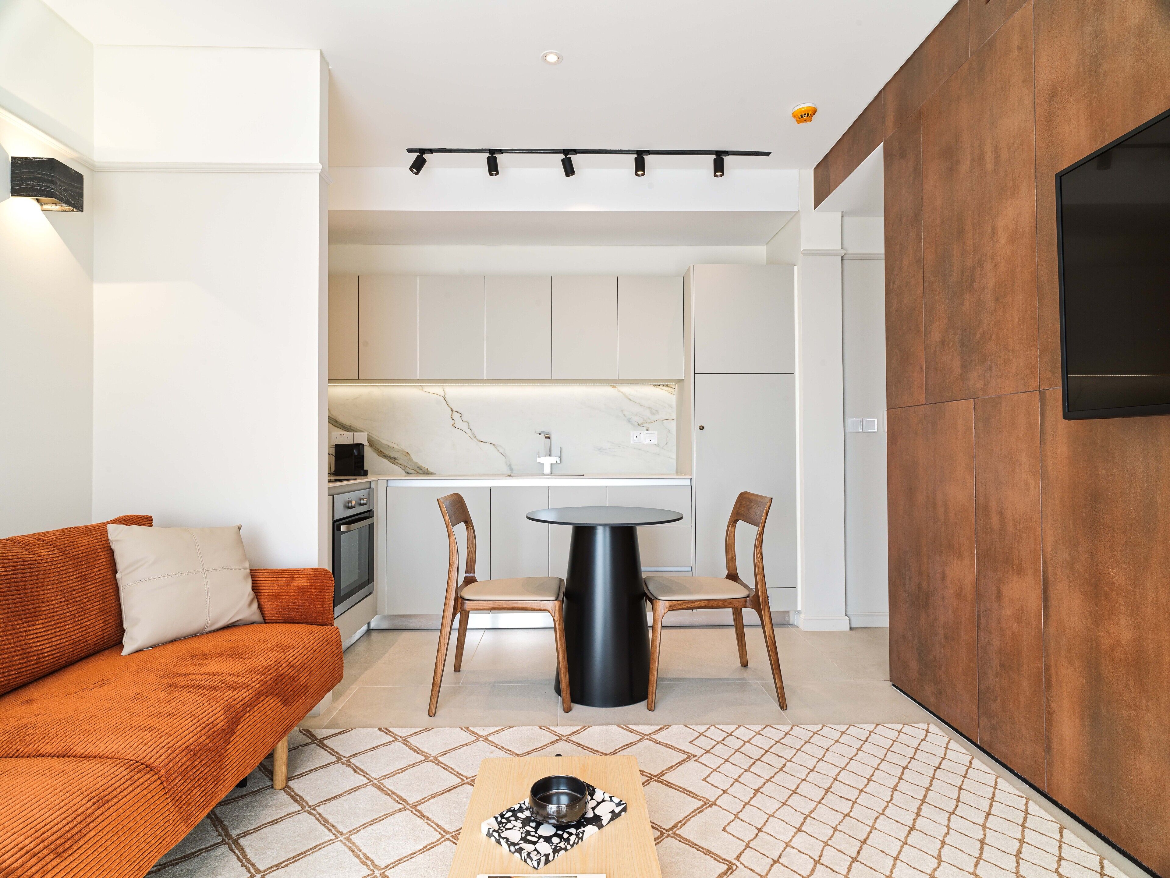 A modern kitchen with white cabinets, a marble countertop, and a dining area with two chairs and a round table.