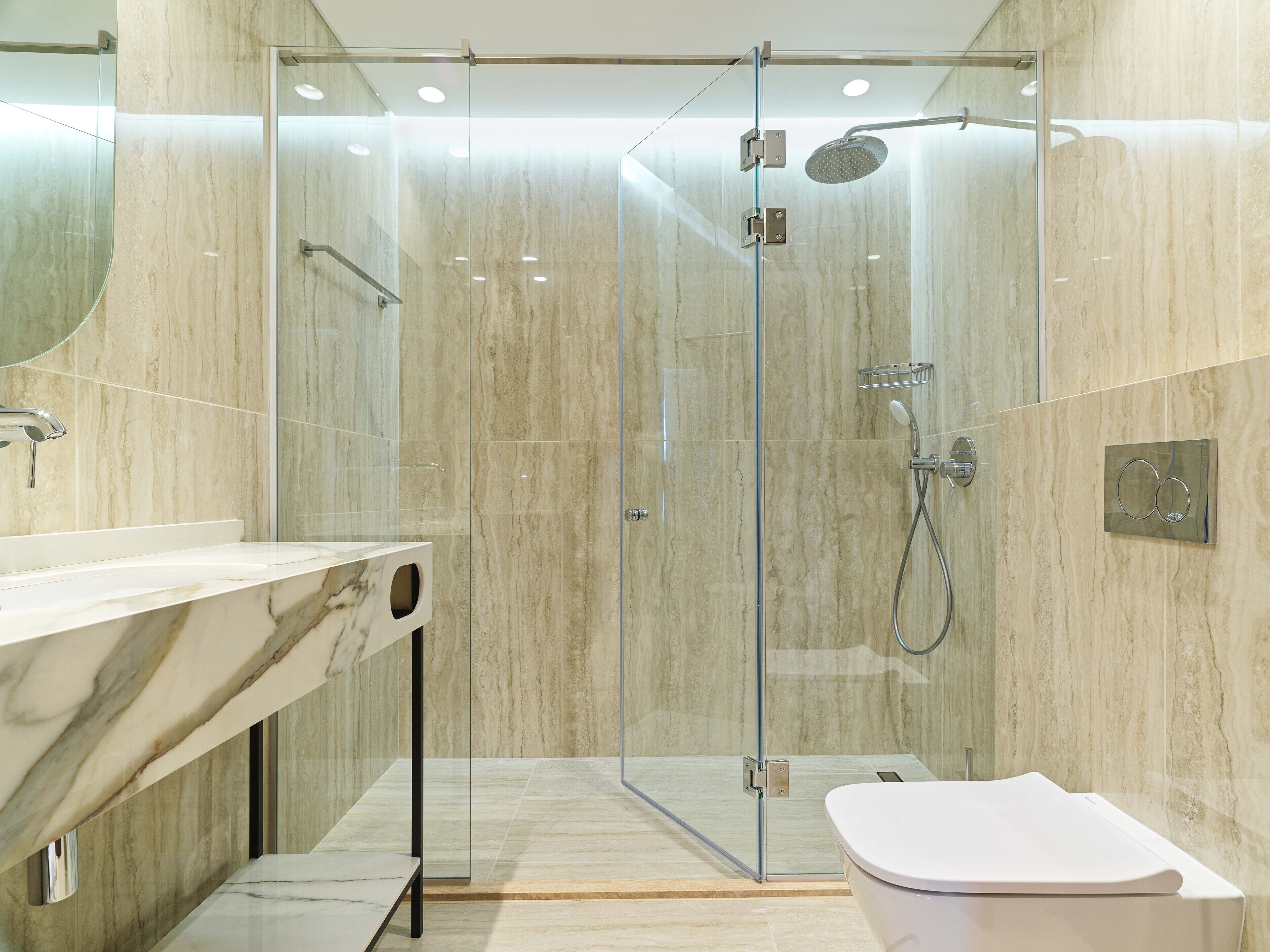 Un baño moderno con ducha de vidrio, tocador de mármol y lavamanos blanco.