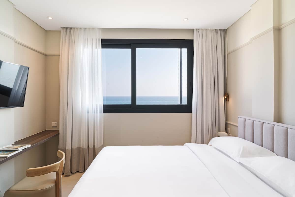 Una habitación de hotel con una cama, un escritorio con silla, televisión y ventana con cortinas.
