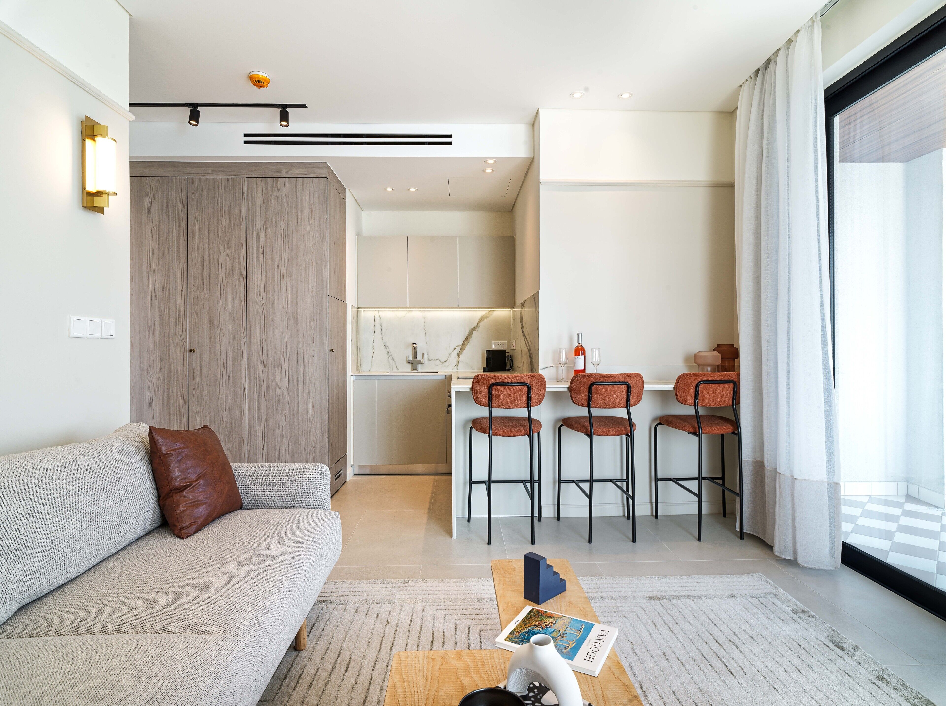 A modern living room with a sofa, a coffee table, and a kitchen area with bar stools.
