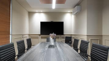 Een vergaderruimte met een lange tafel, zwarte lederen stoelen, een groot flatscreen televisietoestel en een plafondlamp.