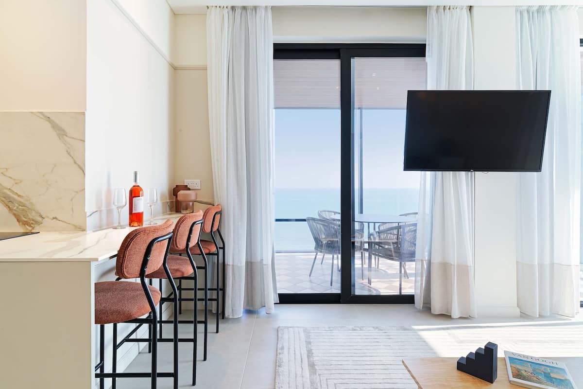 Una habitación de hotel moderna con comedor, televisión de pantalla plana y vista al mar.