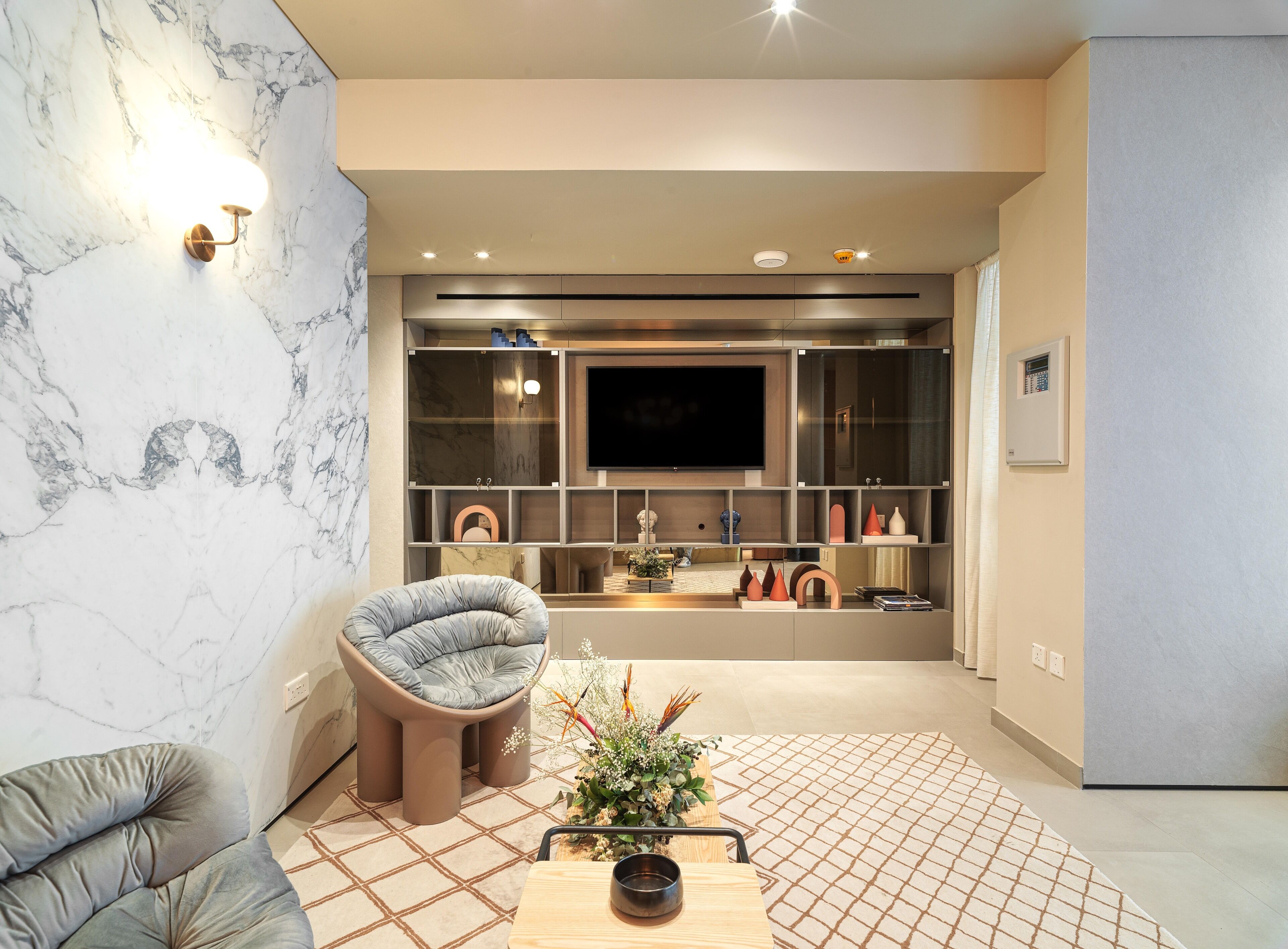 A modern living room with a marble wall, a comfortable seating area, a flat-screen TV, and a built-in shelving unit with decorative items.