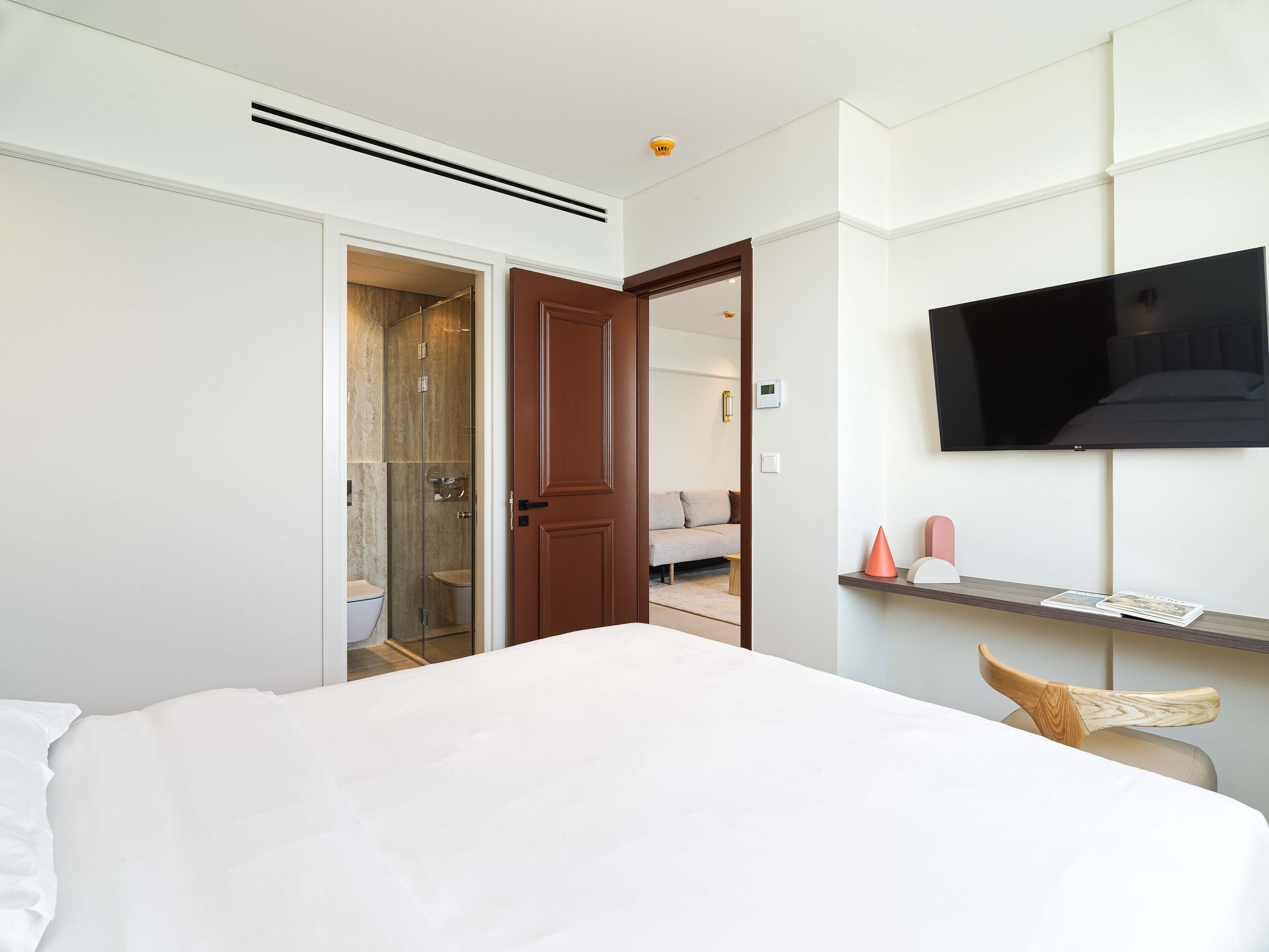 A hotel room with a bed, a TV mounted on the wall, a shower area, and a small seating area with a chair.