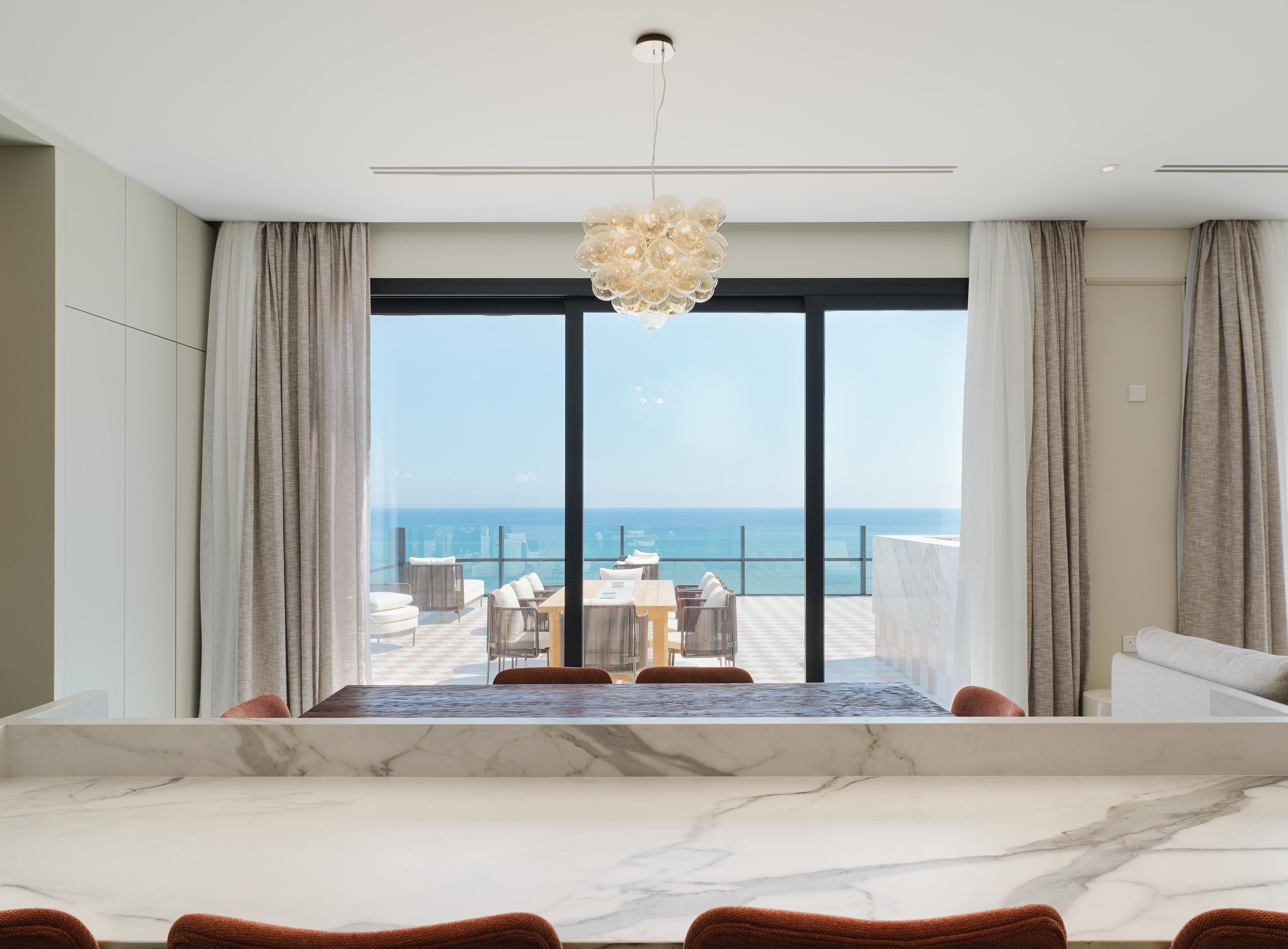 Ein modernes Hotelzimmer mit großem Balkon, einem Esstisch mit Marmorplatte und Blick auf den Ozean.
