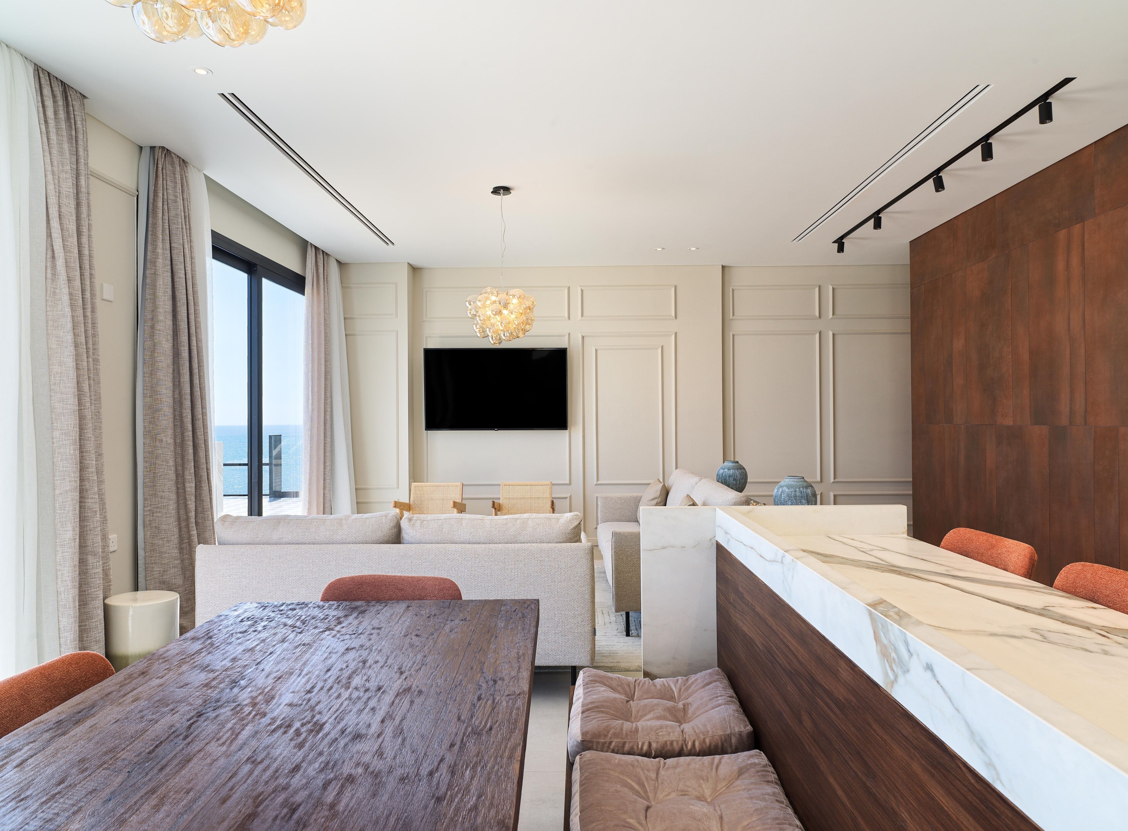 A modern living room with a large wooden table, a sofa, and a marble countertop.