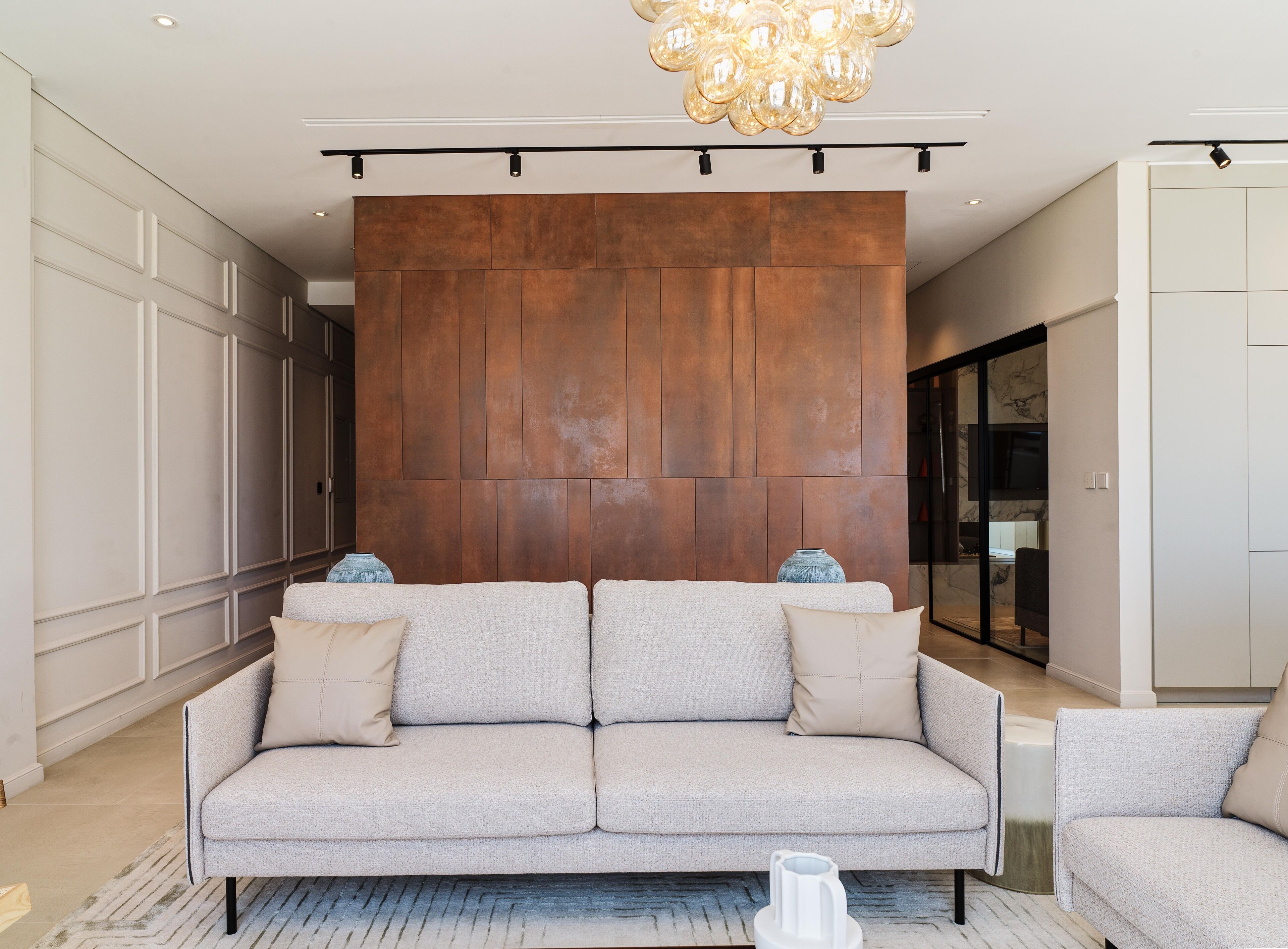 A modern living room with a large sectional sofa, a chandelier, and a marble wall.
