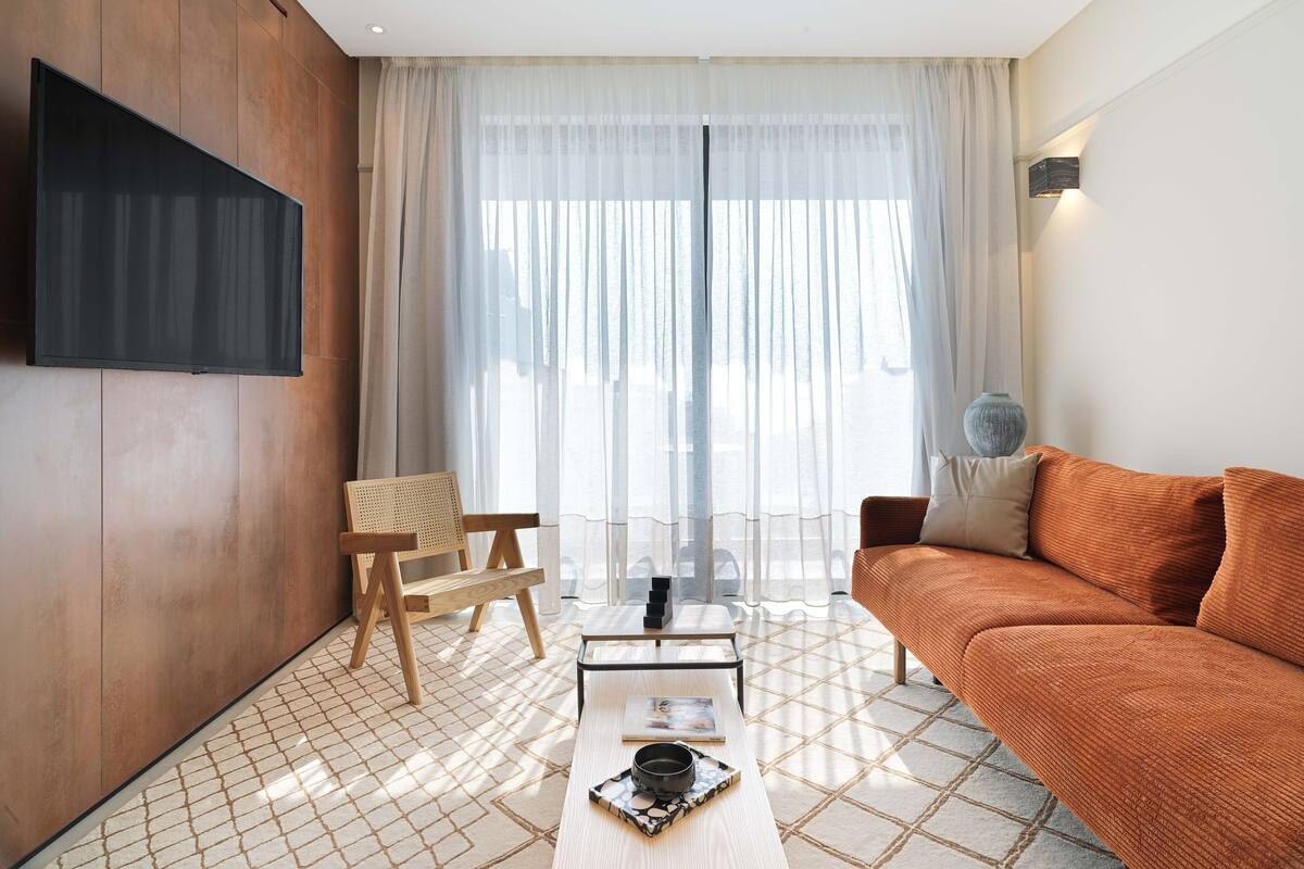 Una sala moderna con un televisor de pantalla plana montado en la pared, una silla de madera, un sofá y una mesa de centro con una bandeja.