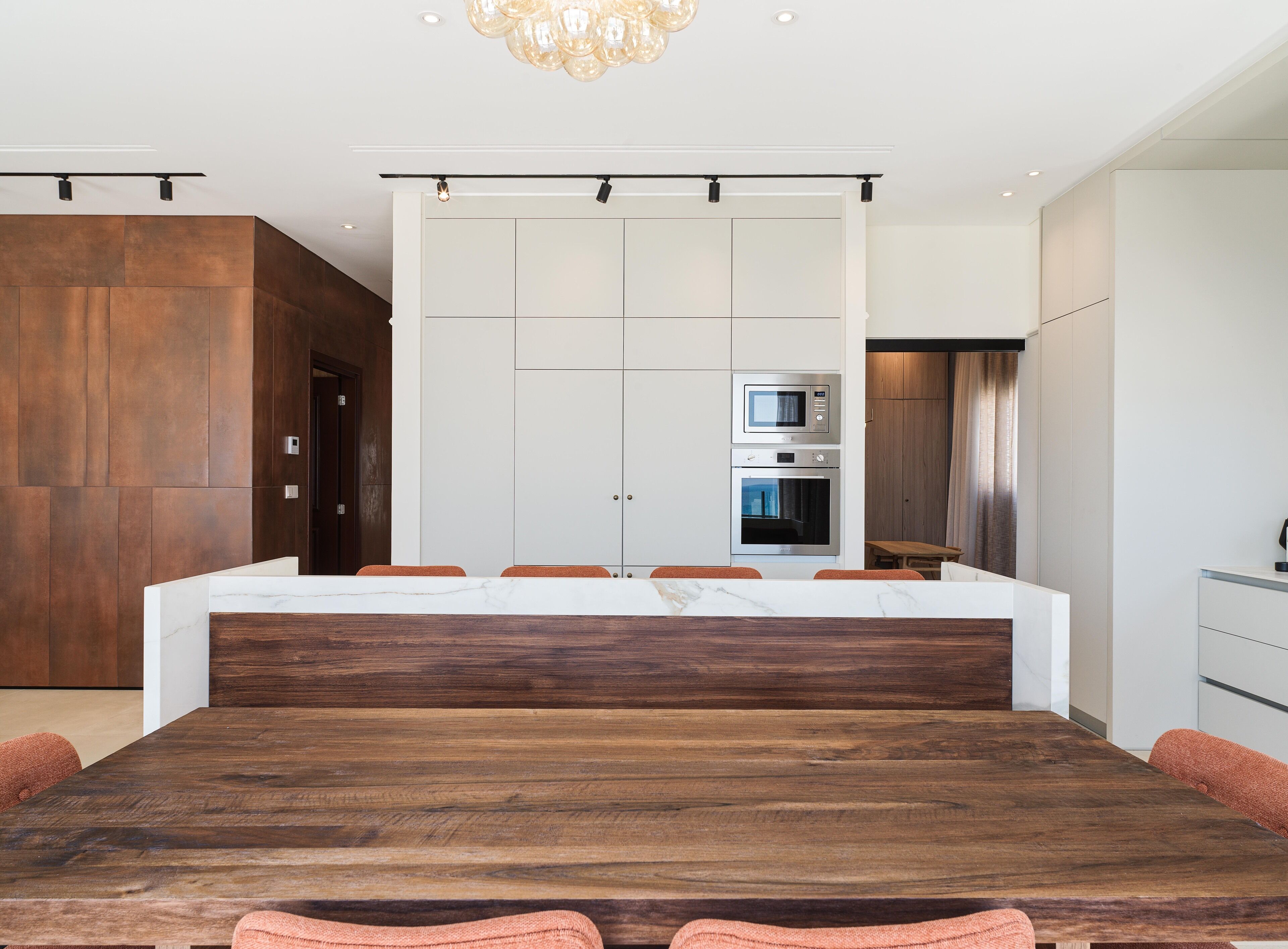 A modern kitchen with built-in appliances, a wooden dining table, and a large island with seating.