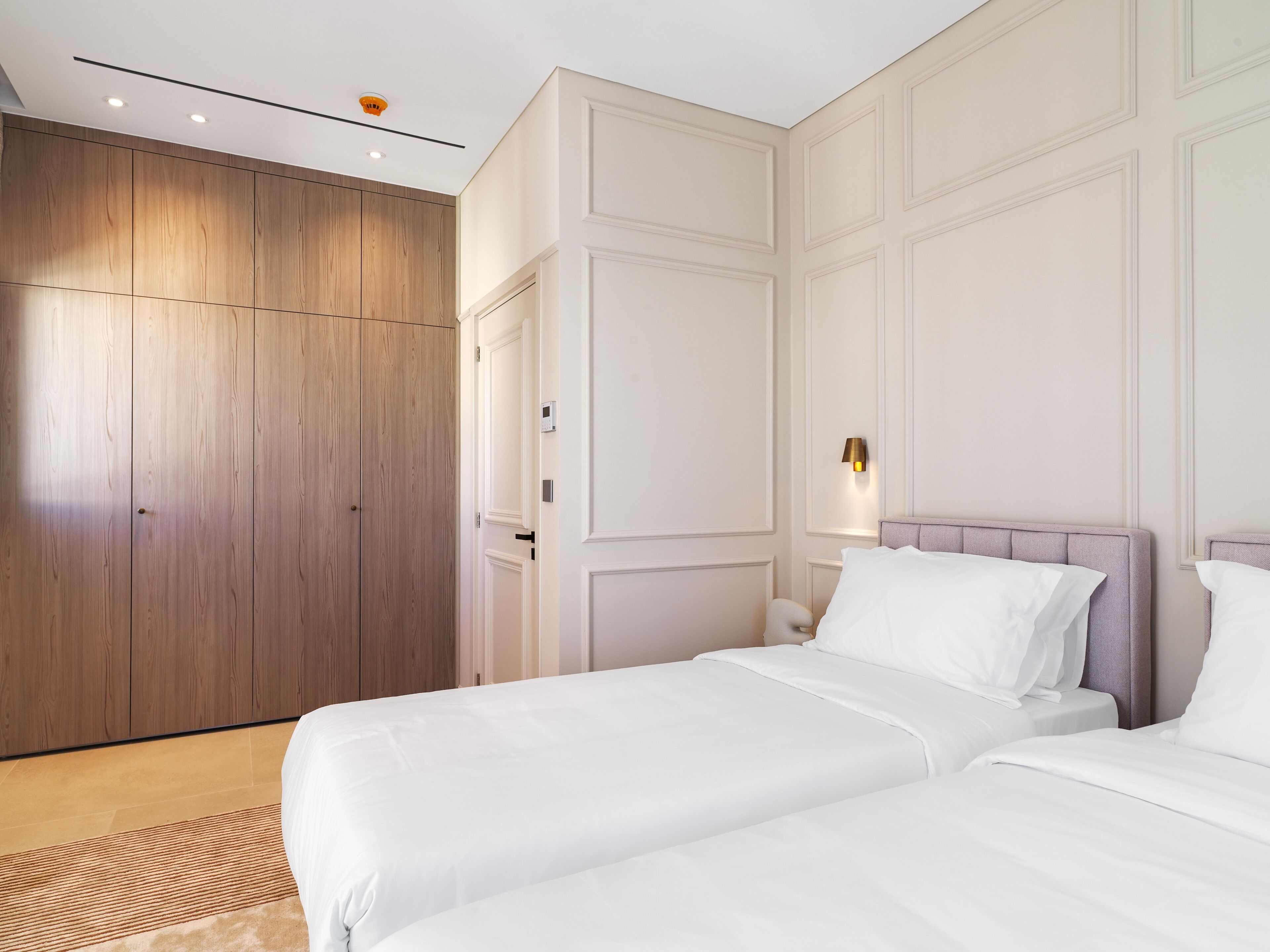 Une chambre d’hôtel dotée d’une grande armoire, d’un lit avec une literie blanche et d’un luminaire fixé au mur.
