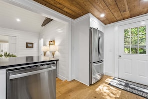 A kitchen with white paneling, a stainless steel refrigerator, a dishwasher, and a wooden ceiling.