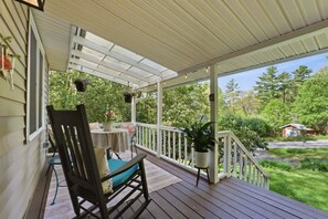 A covered porch with a table and chairs, potted plants, and a view of the surrounding greenery.