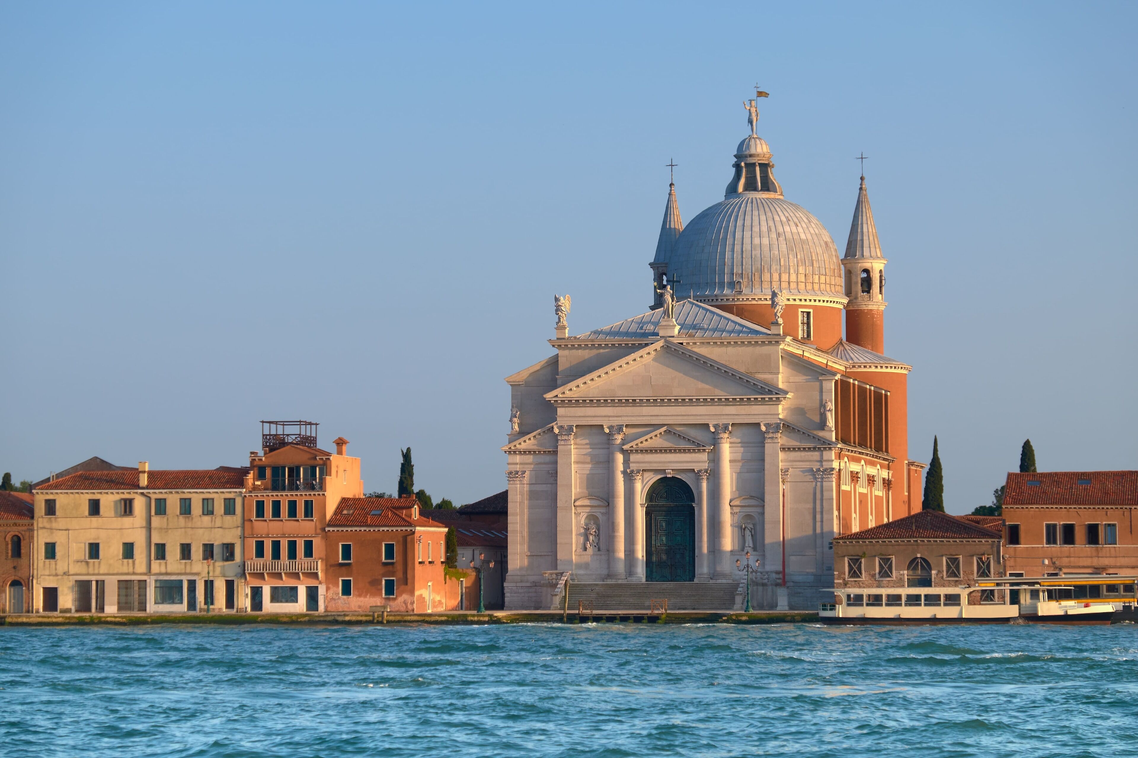 A historic building with a large dome and bell towers, located by a waterfront.