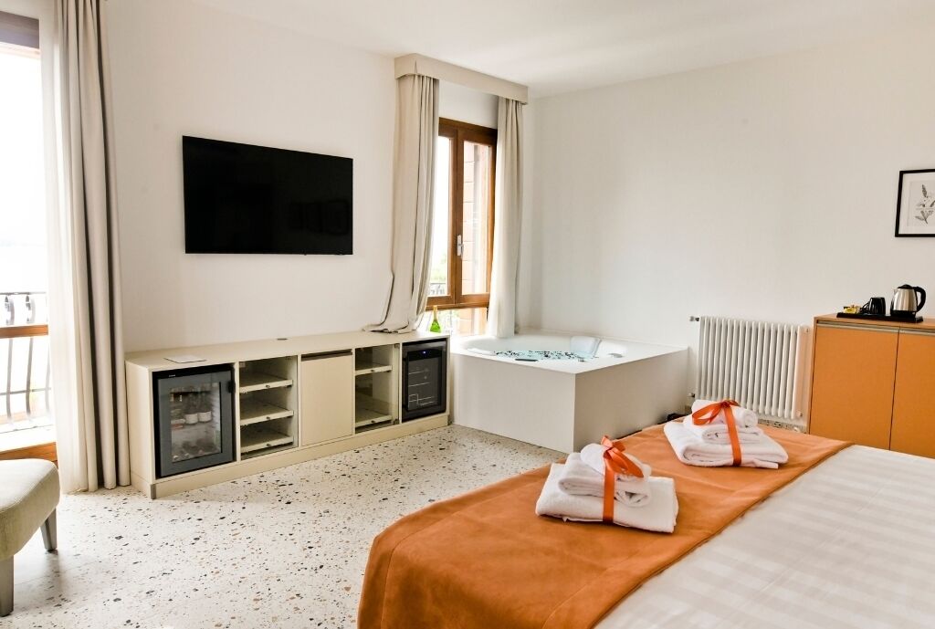 A hotel room with a bed, a desk, a TV, a bathtub, and a window with curtains.