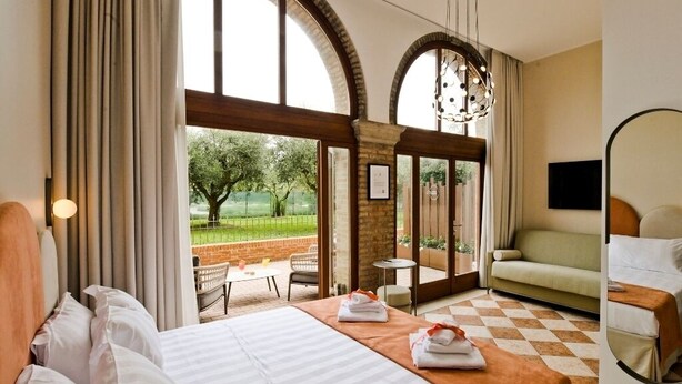 Quarto de hotel com uma cama grande, um sofá, uma TV e uma varanda com vista para o verde.