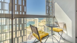 Een balkon met een glazen deur, twee stoelen met gele kussens en een klein rond tafeltje.
