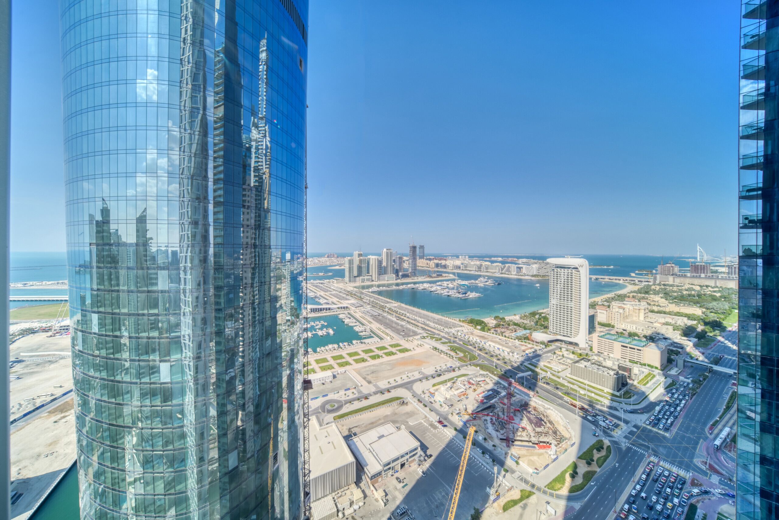 A high-rise building with a glass facade overlooking a marina and cityscape.