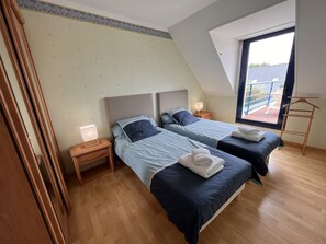 Ein Schlafzimmer mit zwei Betten, Holzboden, einem Nachttisch mit Lampe und einem Fenster mit Blick ins Freie.