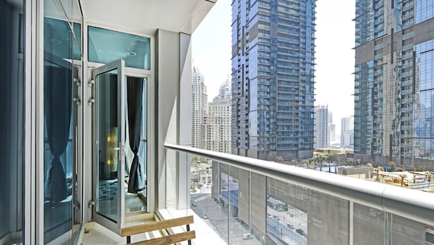 A modern balcony with glass doors, a wooden bench, and a view of high-rise buildings. - Cozy 1BR at Torch Tower Dubai Marina by Deluxe Holiday Homes (Dubai)