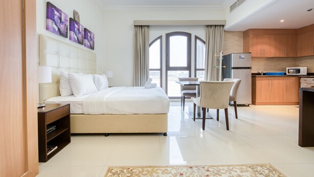 Hotelkamer met een bed, bureau, stoel, kitchenette en een groot raam.