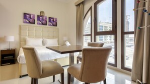 Een hotelkamer met een bed, twee stoelen, een tafel en uitzicht op gebouwen door grote ramen.