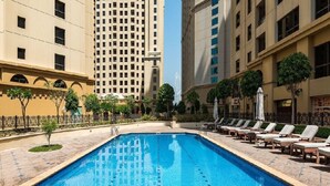 Una piscina con sillas de descanso y una fuente, rodeada de edificios altos.