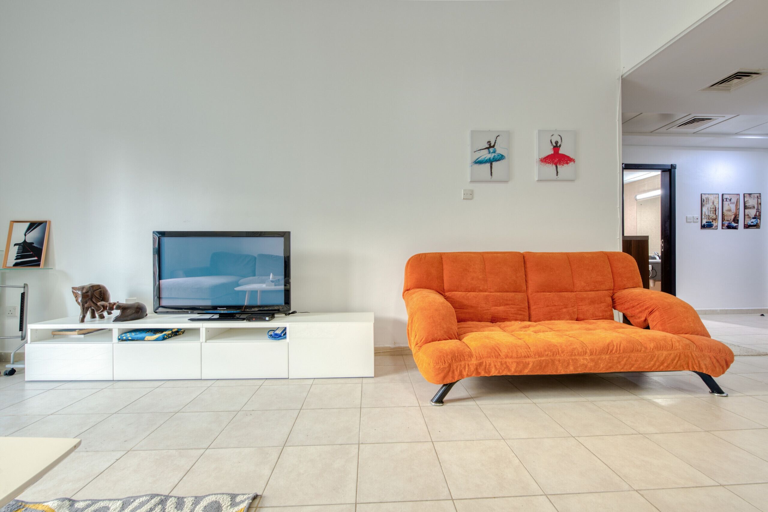Een moderne woonkamer met een grote flatscreen televisie op een witte tv-kast, een oranje bank en een katbeeldje.
