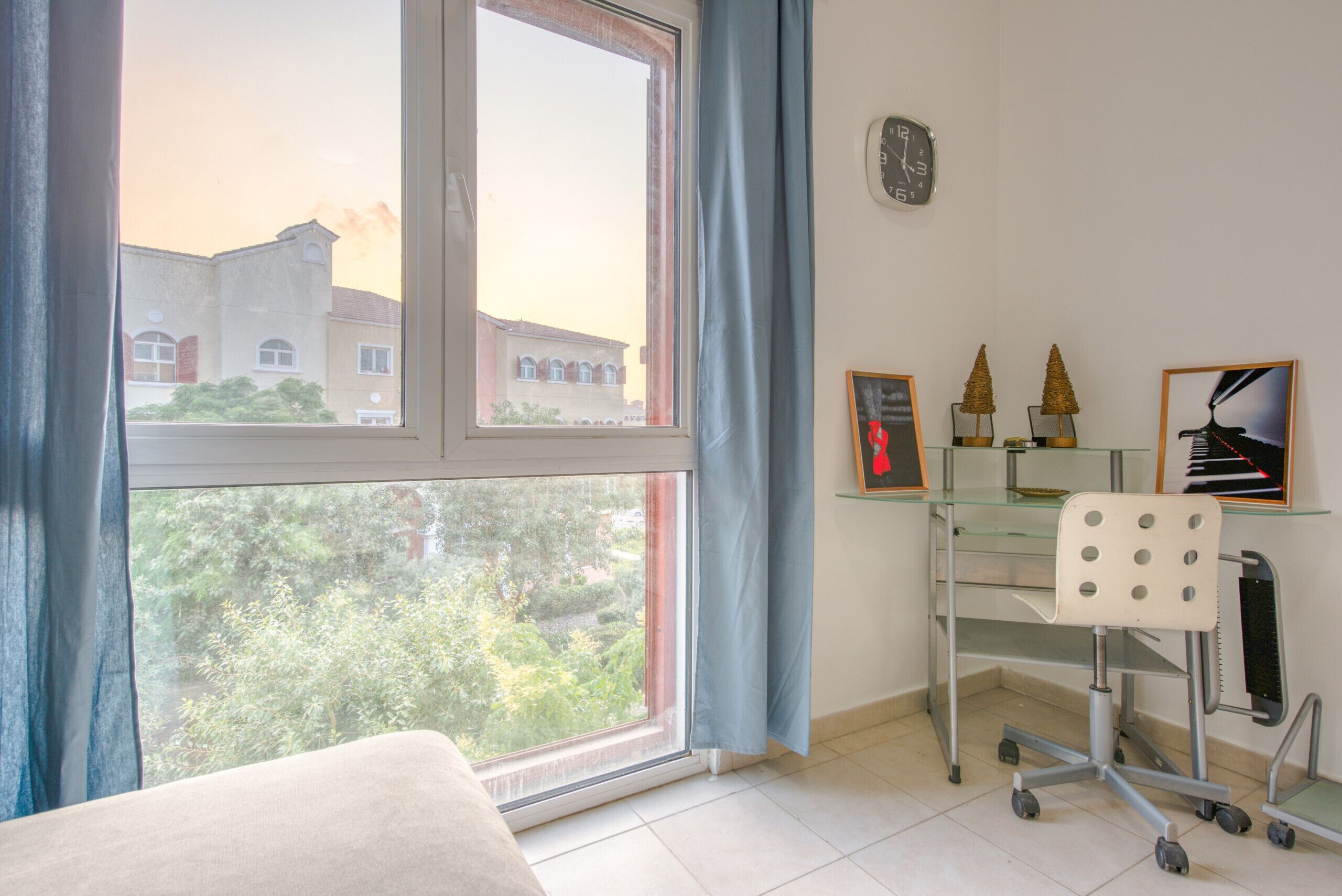 Ein Zimmer mit großem Fenster, Schreibtisch mit Stuhl und einer Uhr an der Wand.