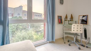 Una habitación con un ventanal grande, un escritorio con silla y un reloj en la pared.