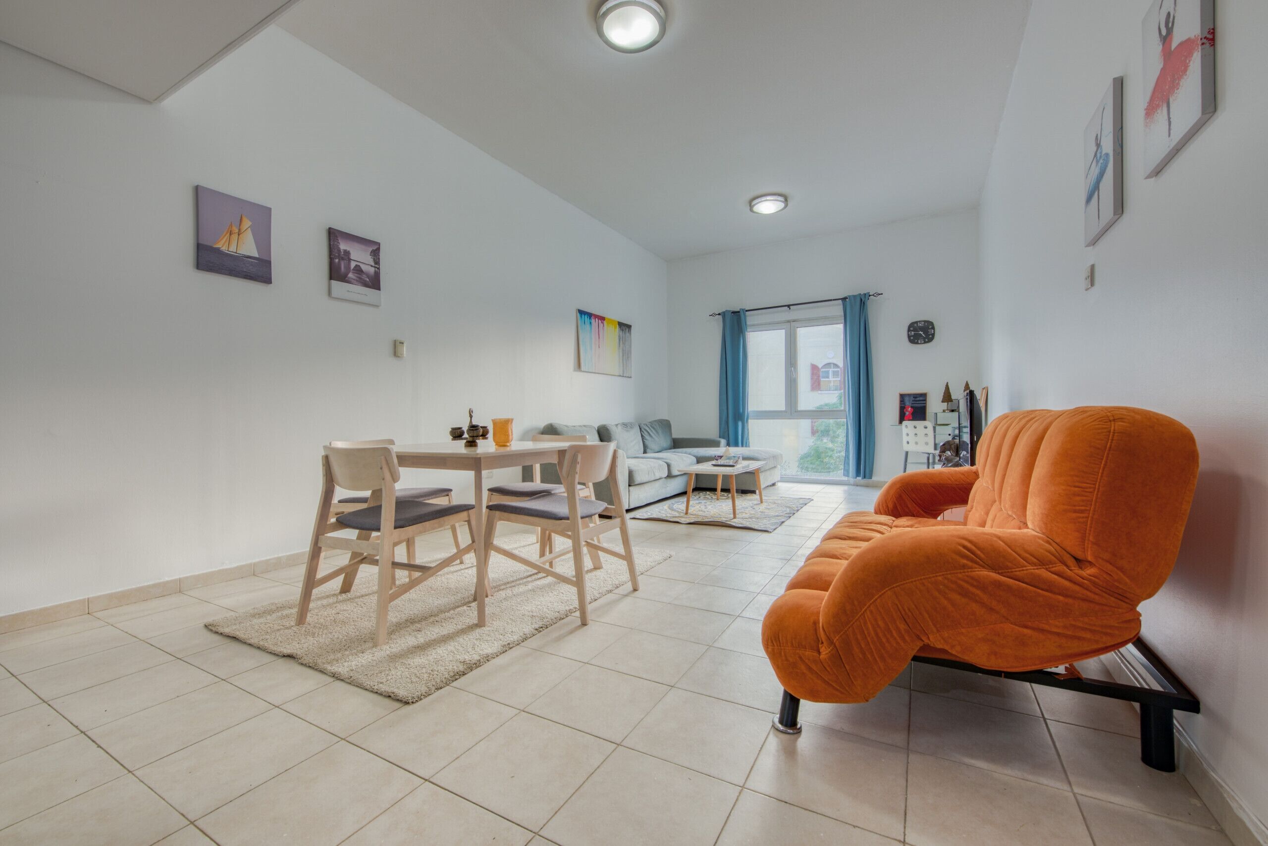 Un saló modern amb zona de menjador, un sofà i una cadira taronja vibrant.