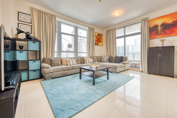 A modern living room with a sectional sofa, a coffee table, and a large window with curtains.