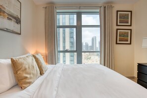 A hotel room with a large bed, two pillows, a window with curtains, and two framed pictures on the wall.