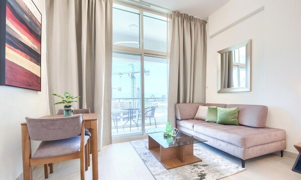 A modern living room with a sofa, a dining table, chairs, and a large window with curtains.