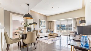 A modern living room with a dining area, a sofa, a TV, and a large window with a city view. - Serene Canal Views from a Spacious Balcony, Just Steps from the Bus Stop (Dubai)