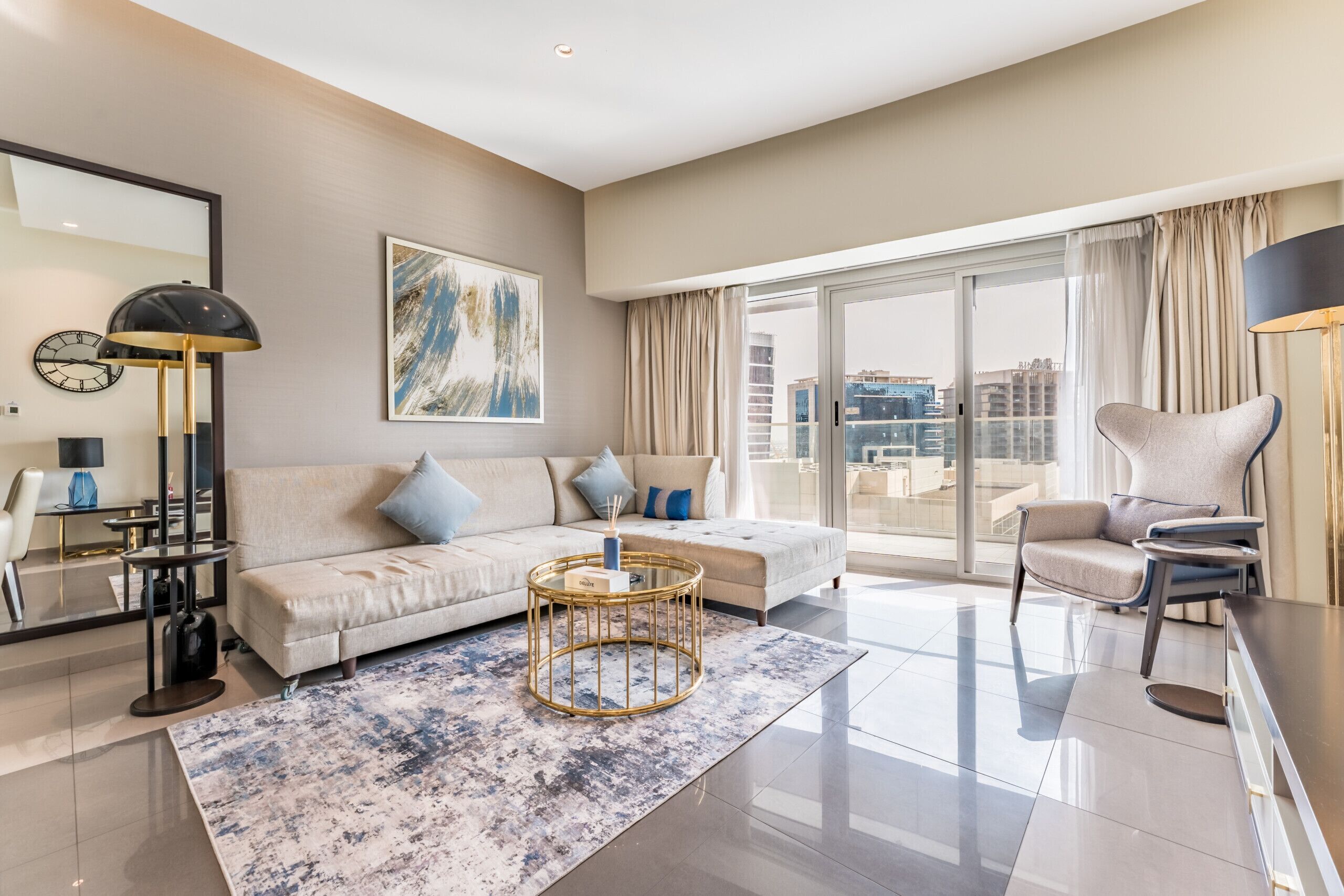A modern living room with a sofa, armchair, and coffee table, large windows with curtains, and a city view.