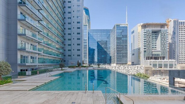 A modern building with a pool, reflecting nearby high-rise structures. - Serene Canal Views from a Spacious Balcony, Just Steps from the Bus Stop (Dubai)