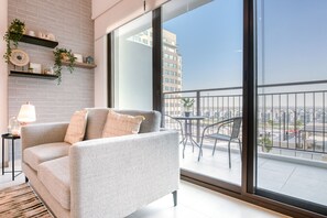 A modern living room with a grey sofa, a small side table, and a balcony with a view of the city.