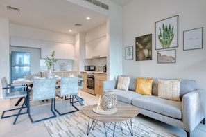 A modern living room with a grey sofa, a coffee table, and a dining area with a table and chairs.