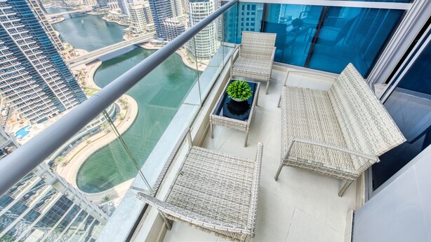 A high-rise balcony with wicker furniture, a potted plant, and a view of a cityscape and water body. - Cozy 1BR at Bay Central 1 Dubai Marina by Deluxe Holiday Homes (Dubai)