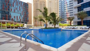 A swimming pool with lounge chairs, surrounded by palm trees and modern buildings. - Cozy 1BR at Bay Central 1 Dubai Marina by Deluxe Holiday Homes (Dubai)