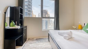 A hotel room with a bed, a desk with a mirror, and a window with a city view. - Cozy 1BR at Bay Central 1 Dubai Marina by Deluxe Holiday Homes (Dubai)