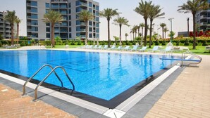 A swimming pool with lounge chairs and palm trees, surrounded by modern buildings. - Exceptional 1BR in MAG 5, Emaar South by Deluxe Holiday Homes (Dubai)